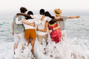 group of young people hugging each other and enjoying sunset at beach
